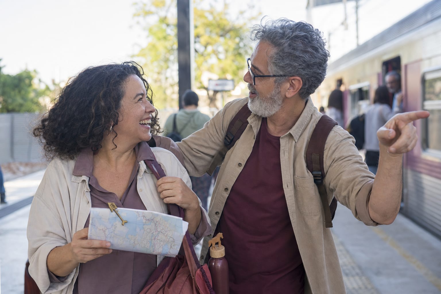 Duas pessoas com mochilas riem e apontam uma rota em uma plataforma de trem